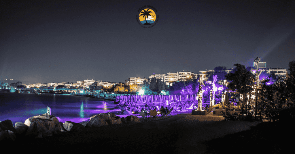 a beach with purple lights and buildings in the background